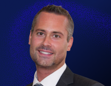 A man in a dark suit and tie smiles at the camera against a textured dark blue background.