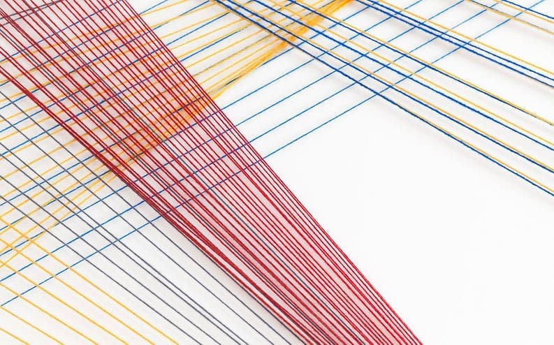 Colorful strings in red, yellow, and blue are arranged diagonally and parallel across a white surface, creating a geometric and abstract pattern with intersecting lines.