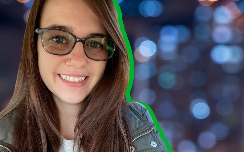 A smiling woman with long brown hair and glasses is in the foreground. She wears a green jacket and a white shirt. The background is blurred with blue and purple bokeh lights. A green outline borders her silhouette.