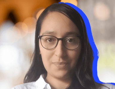 A person with long dark hair and glasses is pictured against a blurred background with warm lights. There is a blue outline around the right side of their head and shoulders.