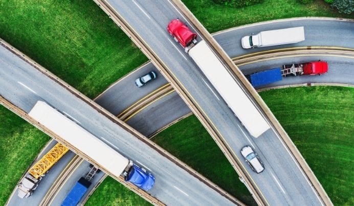 Aerial view of a highway interchange with several large trucks and cars traveling on curved overpasses surrounded by green grass.