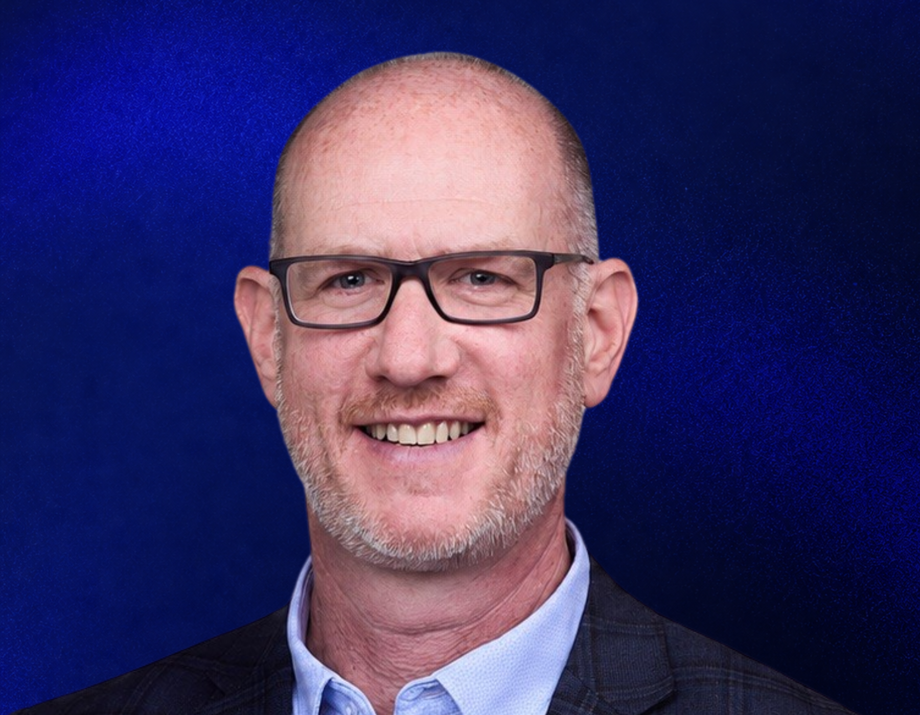 A smiling middle-aged man with glasses, short light hair, and a trimmed beard wearing a checked blazer and light blue shirt, posed in front of a dark blue textured background.