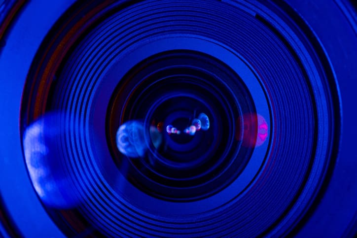 Close-up view of a camera lens with blue and purple reflections and concentric rings in sharp detail, creating an abstract, futuristic effect.