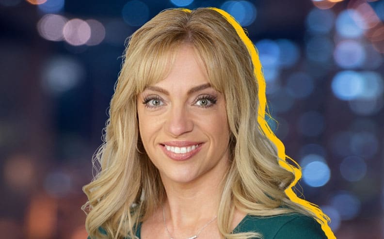 A woman with long blonde hair and a green top smiles at the camera. The background is blurred with blue and orange city lights, and a yellow outline highlights her figure.