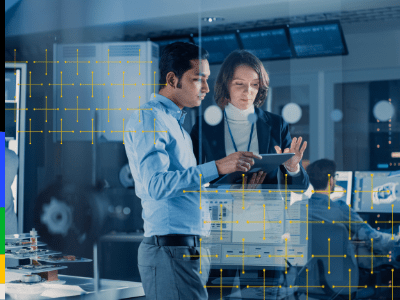 Two people in business attire stand in a modern, high-tech office, looking at a tablet together. Computer monitors and electronic equipment are visible in the background, suggesting a technology or data-focused environment.