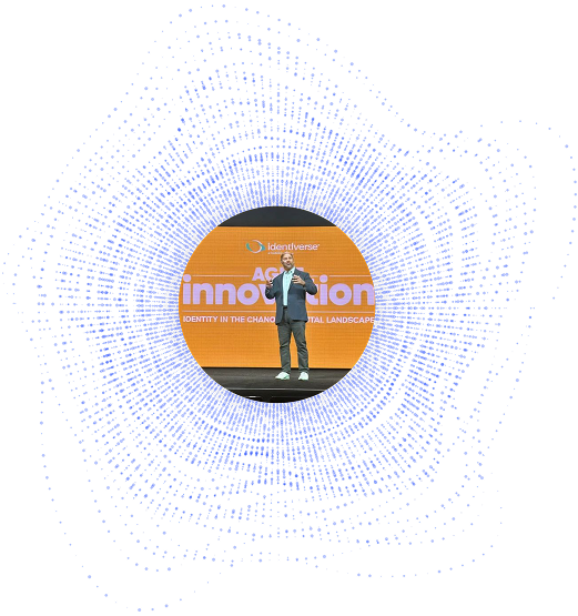 A person stands on stage speaking in front of an orange screen displaying the word innovation, surrounded by a circular blue dotted pattern on a white background.