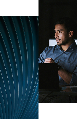 A man in a blue shirt works on a laptop in a dimly lit room; the left half of the image features a blue abstract spiral pattern, symbolizing how we remove roadblocks and streamline processes for effortless maintenance and customization.