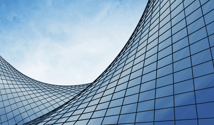 Curved glass building facades with a grid-like pattern reflect the blue sky, creating a modern and abstract architectural scene.