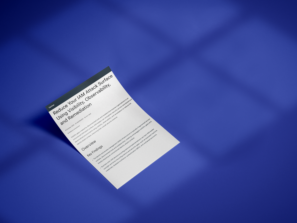 A single sheet of paper with text titled Reduce Your IAM Attack Surface Using Built-in Observability and Remediation lies on a smooth, solid blue surface, with shadows from a window cast across the background.