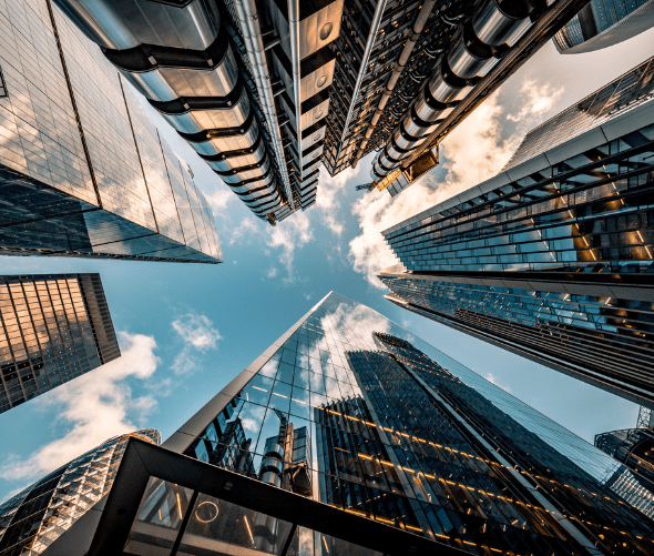 A dramatic upward view of modern skyscrapers with glass and steel facades reflecting the blue sky and clouds, converging towards the center from all sides.
