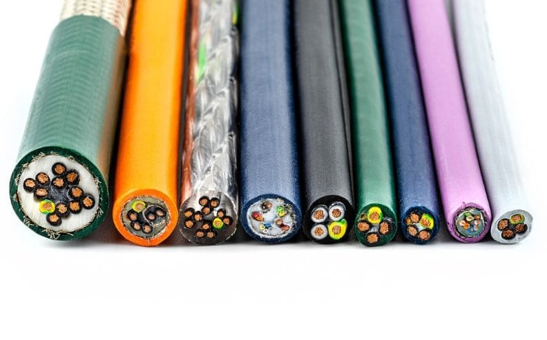 A row of nine electrical cables of varying thickness and color, with exposed cross-sections showing different arrangements of internal wires and insulation.