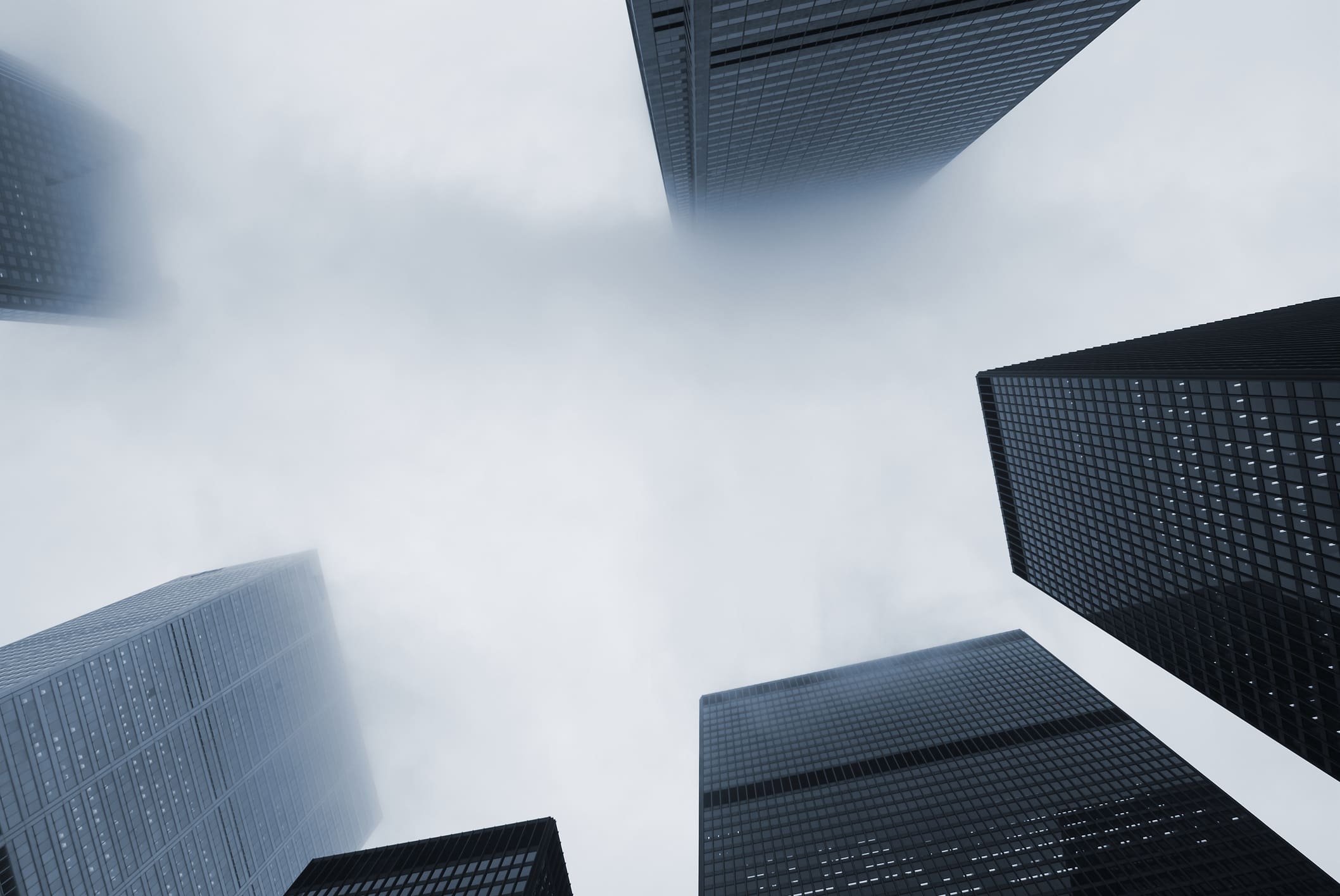 View looking up at tall skyscrapers disappearing into a misty, cloudy sky, creating a dramatic and modern cityscape with buildings on all sides.