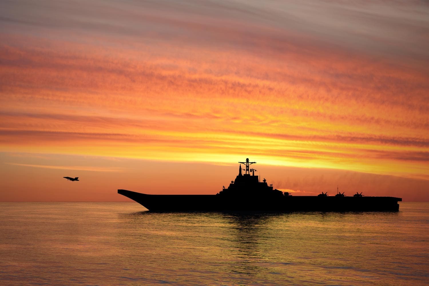 A silhouette of an aircraft carrier and several planes on deck at sunset, with one plane flying nearby over calm ocean waters and a colorful sky.