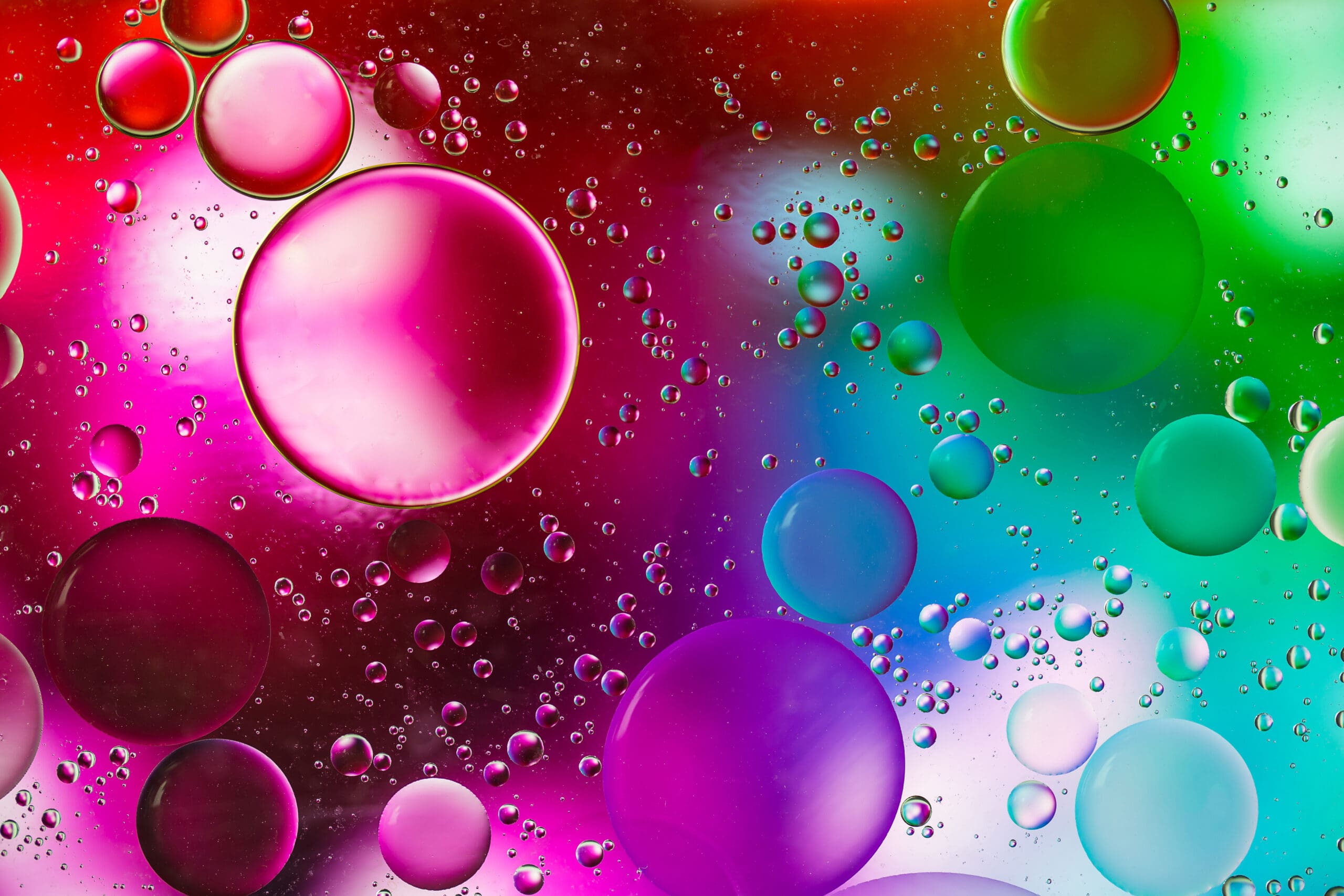 Large and small colorful bubbles in shades of red, pink, green, blue, and purple float against a vibrant, multicolored background. The image has an abstract, dreamy appearance with soft gradients and glowing effects.