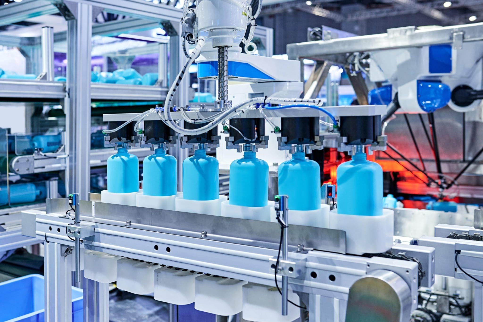 Automated production line filling blue liquid into plastic bottles using robotic machinery in a modern industrial facility.