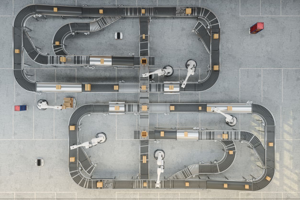 Aerial view of an automated conveyor belt system with robotic arms sorting brown packages in a warehouse, with a red vehicle in the upper right and blue vehicle in the lower left.