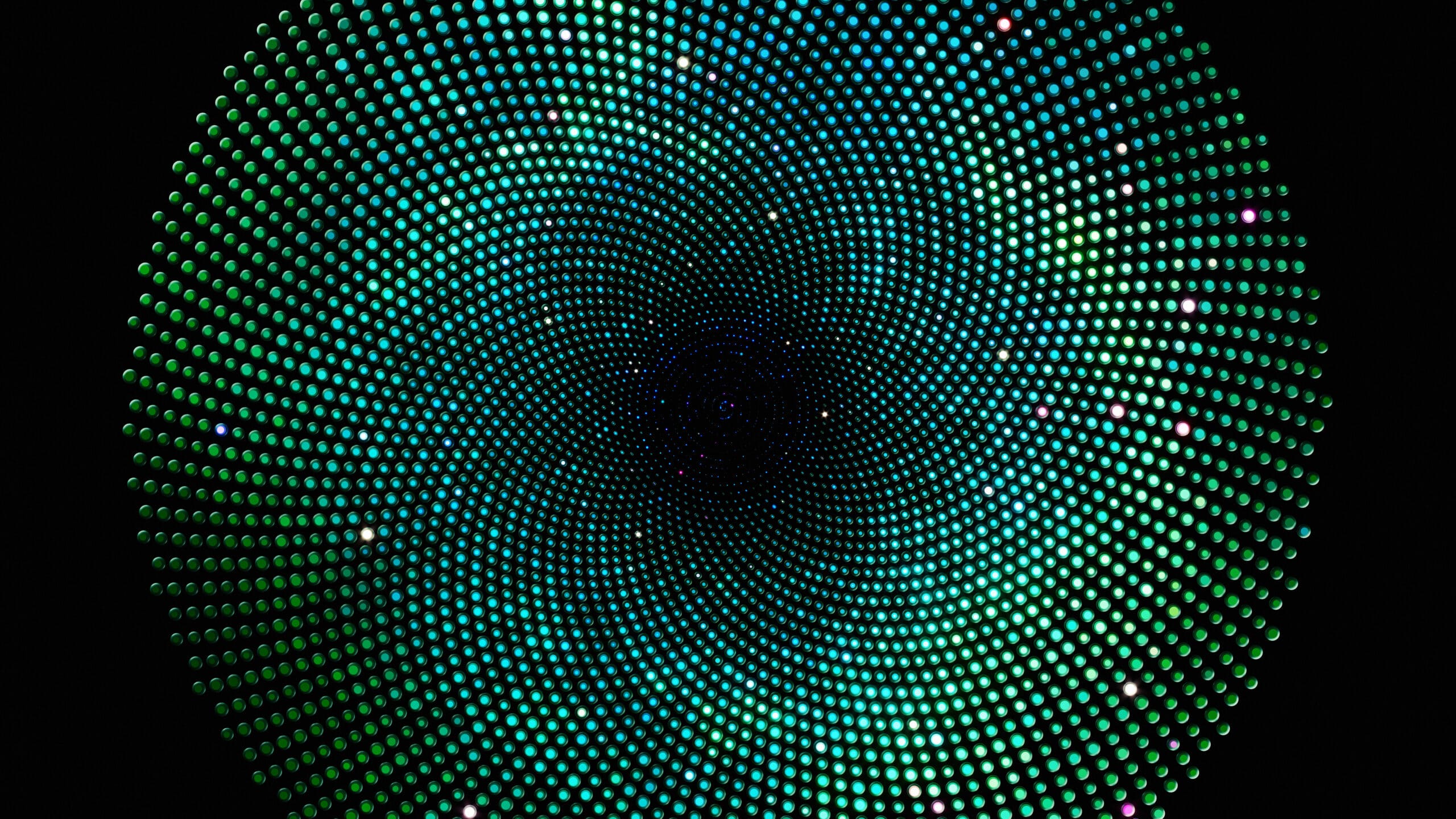 A spiral pattern of teal and green dots against a black background, creating a hypnotic, swirling visual effect with a glowing, digital appearance.
