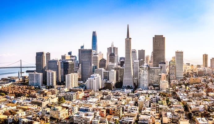A bright, clear view of San Francisco’s downtown skyline featuring modern skyscrapers, the Transamerica Pyramid, and the Bay Bridge in the background against a blue sky.