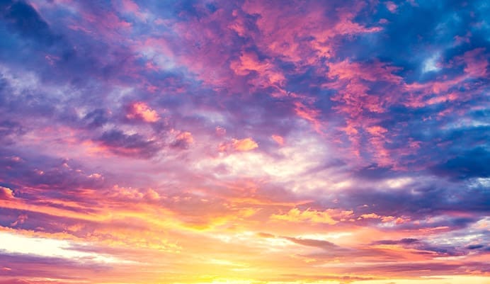 Vibrant sunset sky with dramatic clouds in shades of pink, purple, orange, and blue, as the sun sets near the horizon, casting colorful light across the sky.